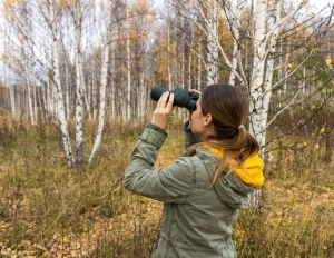 Young woman with binoculars watching birds in the autumn forest Scientific research - Songbird RV Park 2